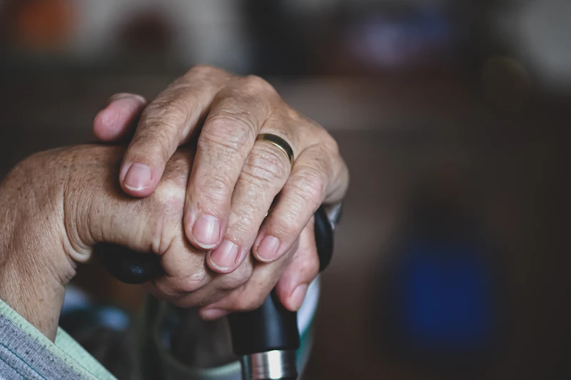 An older person&rsquo;s hands resting on a walking stick