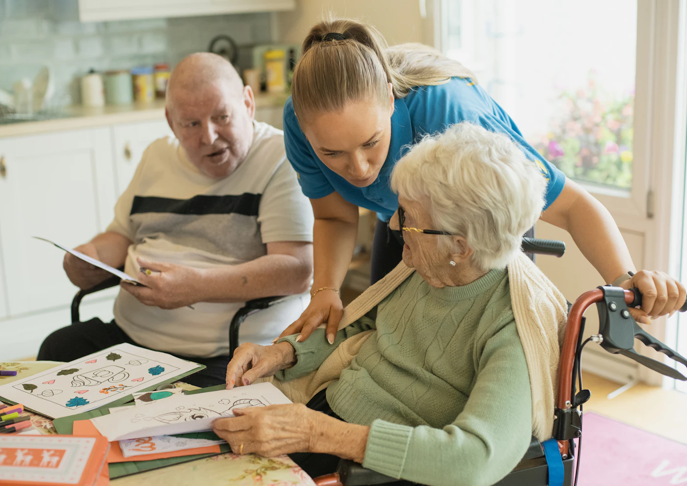A carer sitting with an older couple at their kitchen table, sharing an activity