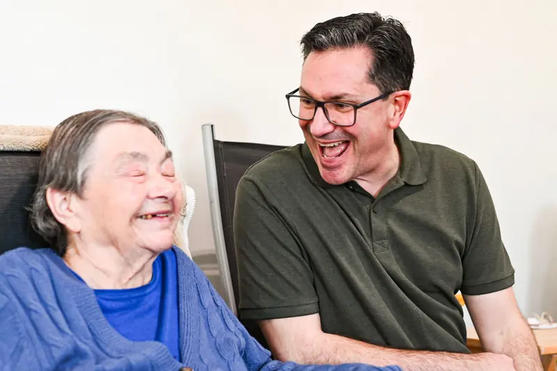 A carer and an older woman laughing together at home